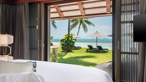 A hotel room with a bed, a TV, and a view of the beach with lounge chairs and umbrellas. - Villa Akatsuki (Koh Samui)