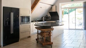 A kitchen with a black refrigerator, a microwave, a wooden cart, and a large island.