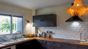 A modern kitchen with dark cabinetry, a white tiled backsplash, a wooden countertop, and a unique hanging light fixture. - Spacious 5-Bedroom House with Private Pool, Games Room, and Terrace in Changé (Changé)