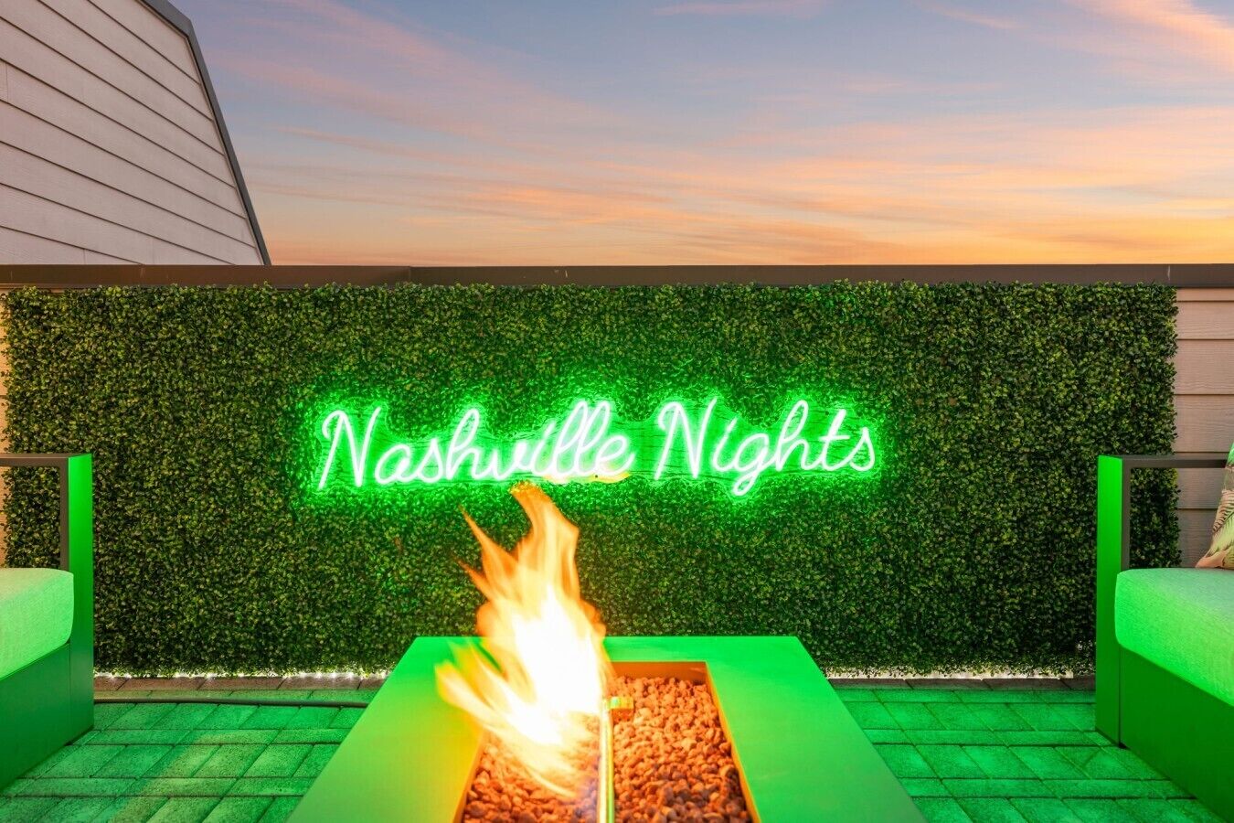A neon sign reading 'Nashville Nights' against a green wall, with a fire feature in the foreground.
