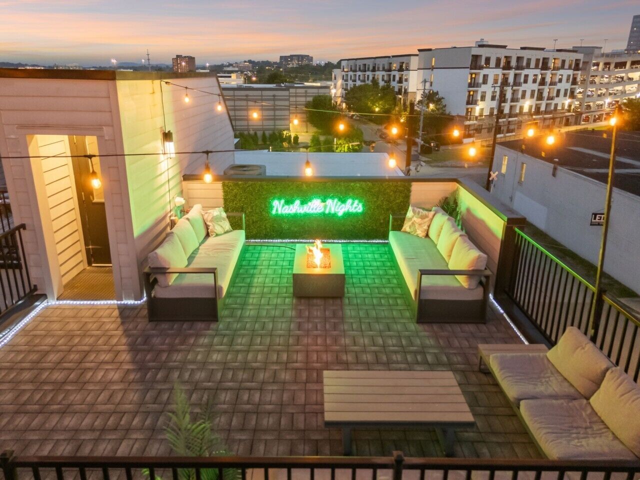 An outdoor seating area with a neon sign, a fire feature, and a view of the cityscape.