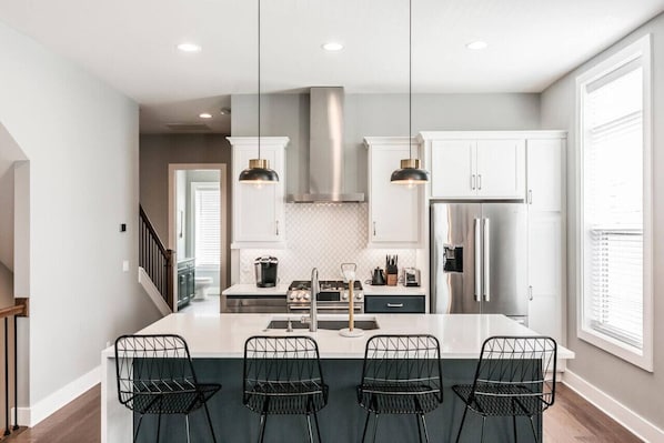 A modern kitchen with a central island, pendant lighting, and a stainless steel range hood.