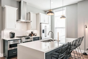 A modern kitchen with white cabinetry, stainless steel appliances, and a central island with bar stools.