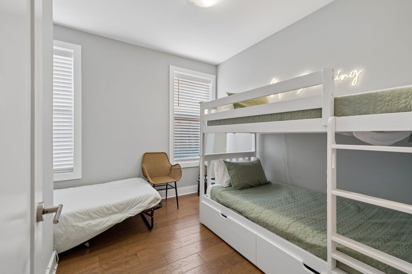 Une chambre avec des lits superposés, une chaise et une fenêtre avec des stores.