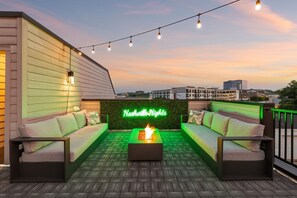 An outdoor seating area with a neon sign, a fire feature, and a view of the cityscape.