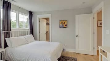 A bedroom with a bed, a bedside table, a nightstand, a window with curtains, and a door leading to a bathroom.