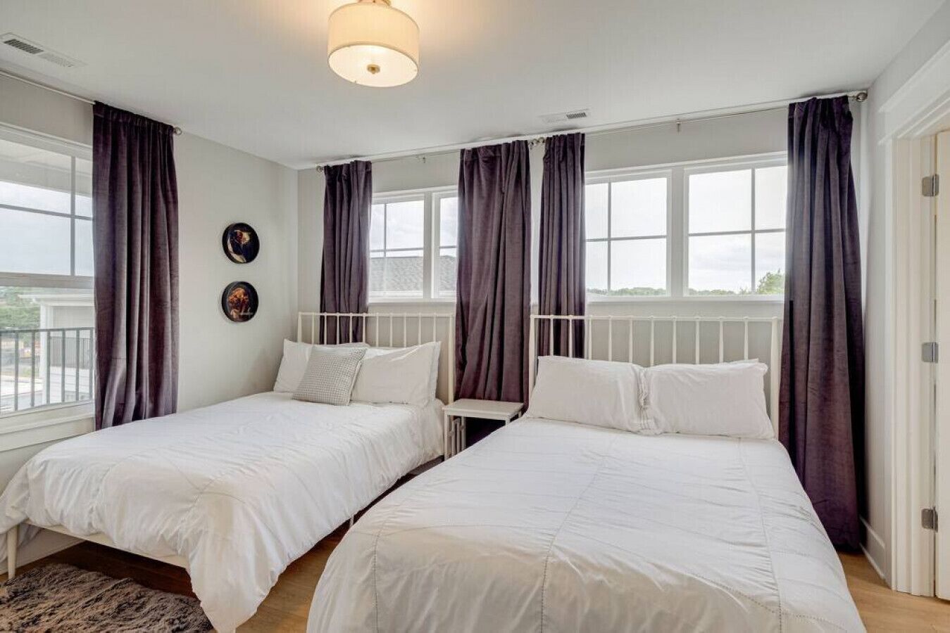 Une chambre d’hôtel avec deux lits simples, une grande fenêtre avec des rideaux, un luminaire au plafond et un petit tapis.