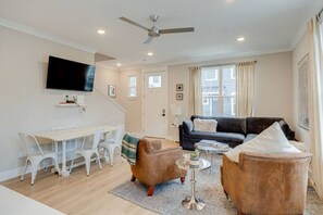 Un salon moderne doté d’un téléviseur à écran plat, d’un canapé, de deux fauteuils, d’une table basse et d’un coin repas avec une table et des chaises blanches.