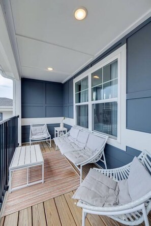 Un espace extérieur aménagé, abrité et doté de mobilier en osier blanc et d’un plancher en bois.