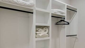 A walk-in closet with multiple shelves and hanging space, featuring neatly folded towels and a black hanger.