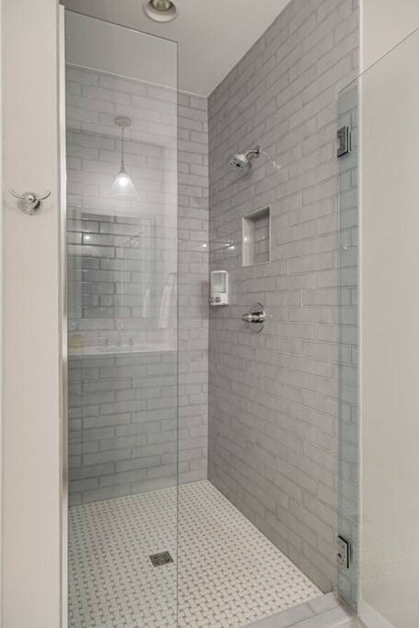 Lasiseinöillä varustettu suihku, jossa on laatoitettu lattia ja pieni peili.