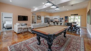 Un salón espacioso con mesa de billar, un conjunto de sofás, televisor y una zona de cocina con mesa y sillas de comedor.