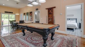 Una habitación amplia con mesa de billar, un rack de billar y una puerta que da a un dormitorio.