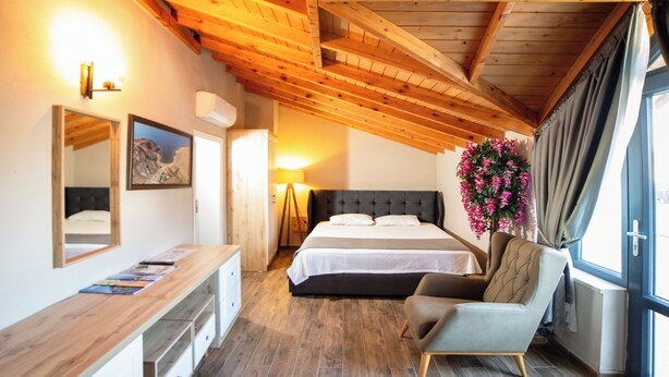 Un dormitorio con techo de madera, una cama con ropa de cama blanca, una mesita de noche, una silla, un espejo y una ventana con cortinas.