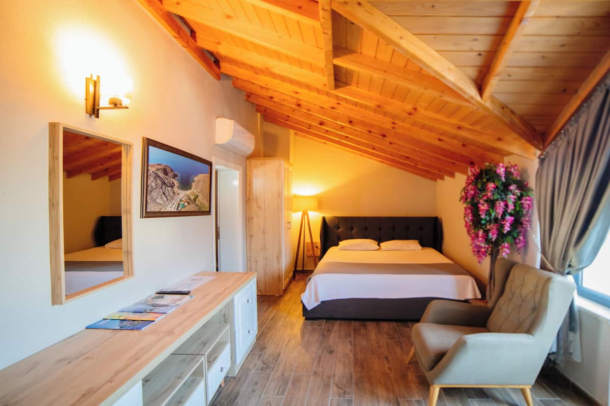 A bedroom with a wooden ceiling, a bed, a bedside table, a chair, a mirror, and a wall-mounted air conditioner.