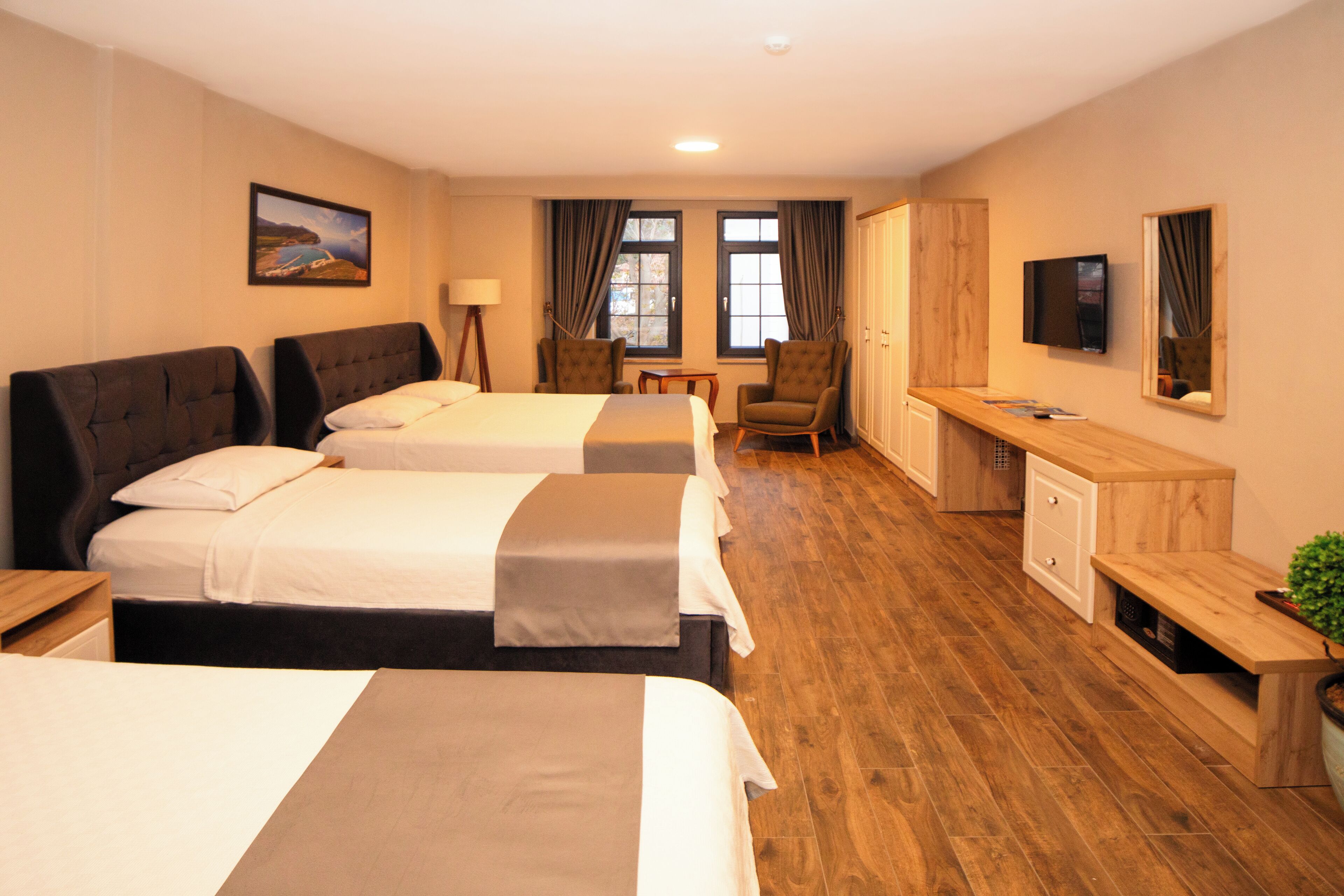 A hotel room with three beds, a desk, a chair, a television, and a cabinet.