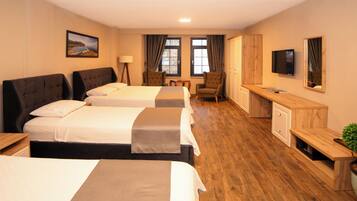 A hotel room with three beds, a desk, a chair, a television, and a cabinet.