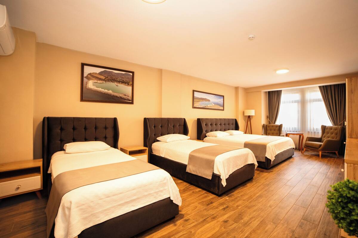 A hotel room with three beds, wooden flooring, and two framed pictures on the wall.