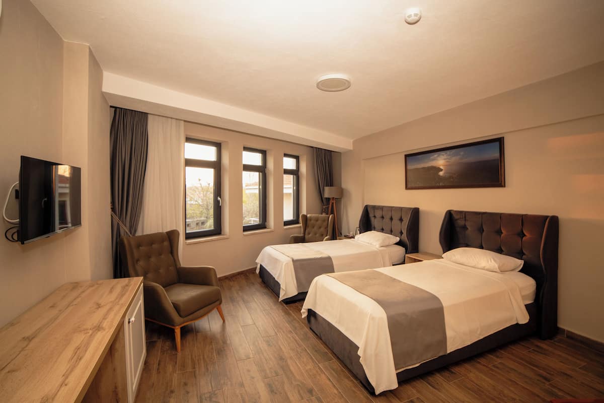 A hotel room with two beds, a desk, a chair, a TV, and a painting on the wall.