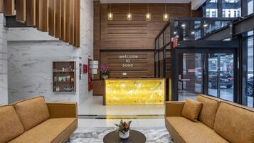 A modern lobby with a reception desk, sofas, a marble floor, and a view of the street through large windows.