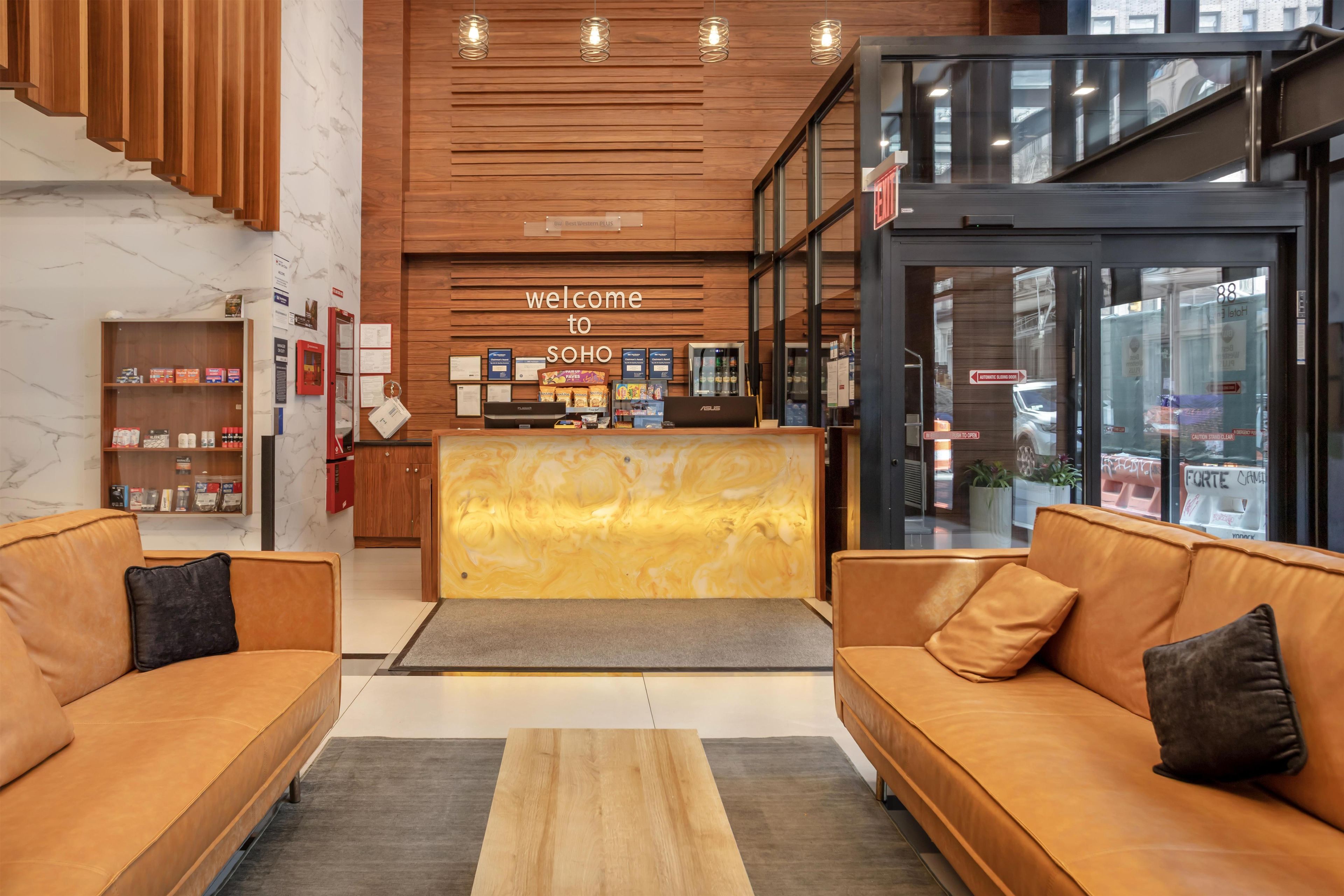 A modern hotel lobby with a reception desk, sofas, a wooden wall, and a glass door leading outside.
