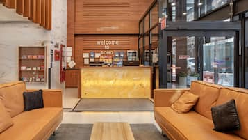 A modern hotel lobby with a reception desk, sofas, a wooden wall, and a glass door leading outside.