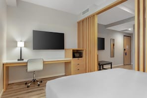 A hotel room with a bed, a desk with a chair, a flat-screen TV, a small table with a chair, and a wooden partition. - Best Western Plus Soho Hotel (New York)