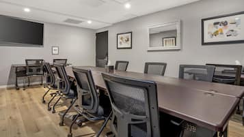 A conference room with a long table, multiple chairs, a projector screen, and framed artwork on the walls.