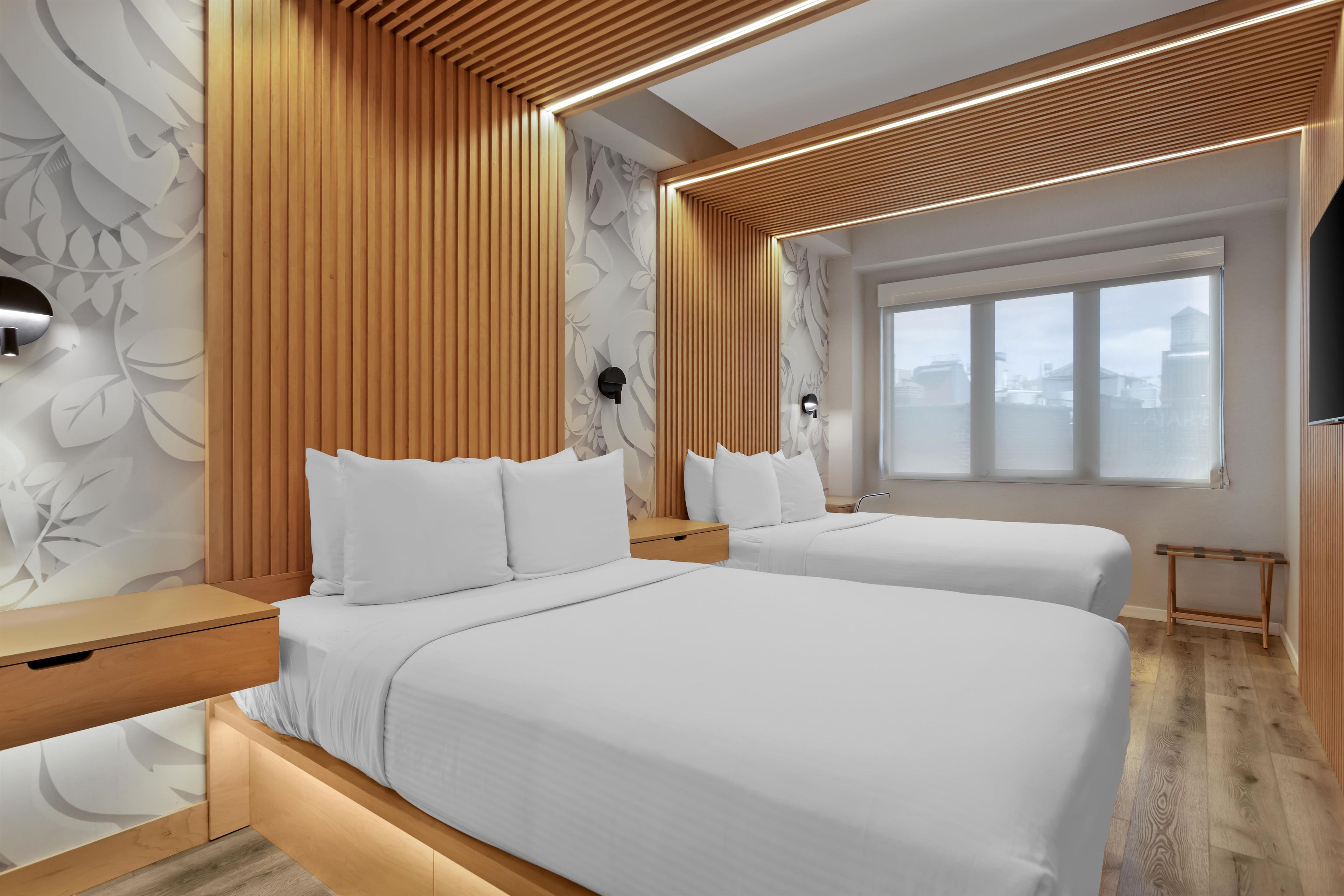 A hotel room with two beds, wooden paneling, a large window, and a city view.