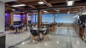 A modern dining area with multiple tables and chairs, a kitchen counter, and a large window providing a view of the outside. - Best Western Plus Soho Hotel (New York)