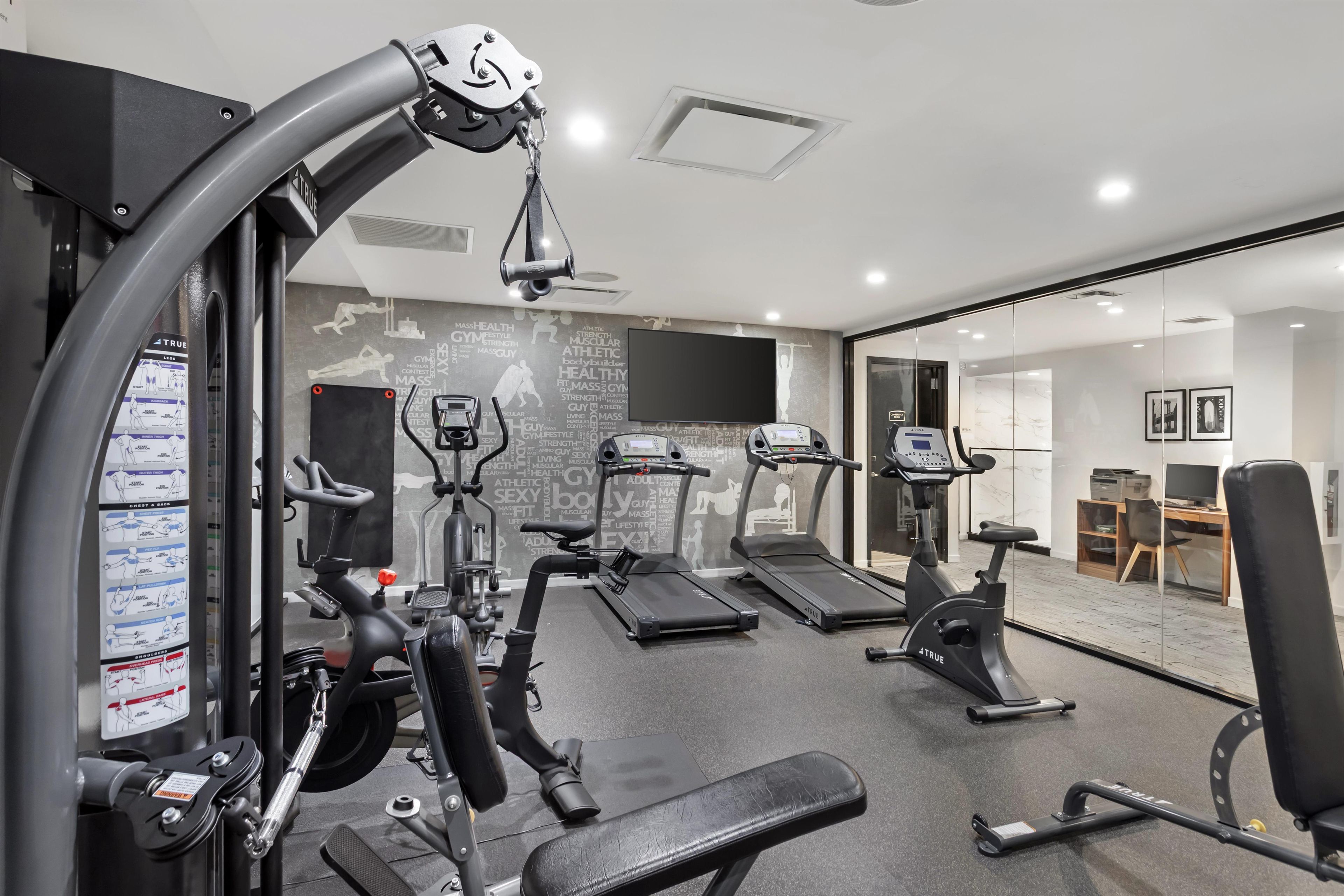 Une salle de sport moderne équipée de divers appareils d’exercice, notamment des tapis de course, un vélo elliptique et des appareils de musculation.