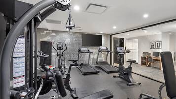 Une salle de sport moderne équipée de divers appareils d’exercice, notamment des tapis de course, un vélo elliptique et des appareils de musculation.