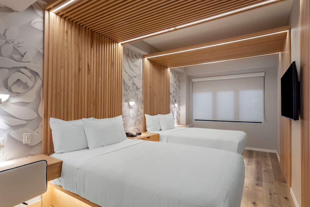 A modern hotel room with two beds, wooden paneling, a large mirror, and a flat-screen TV.