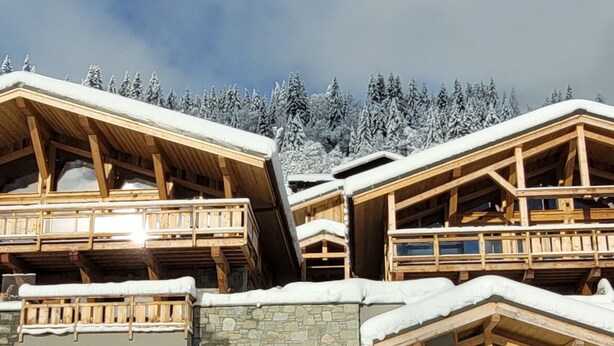 Eine Holzhütte mit Steinfundament, mehreren Balkonen und Blick auf schneebedeckte Bäume.