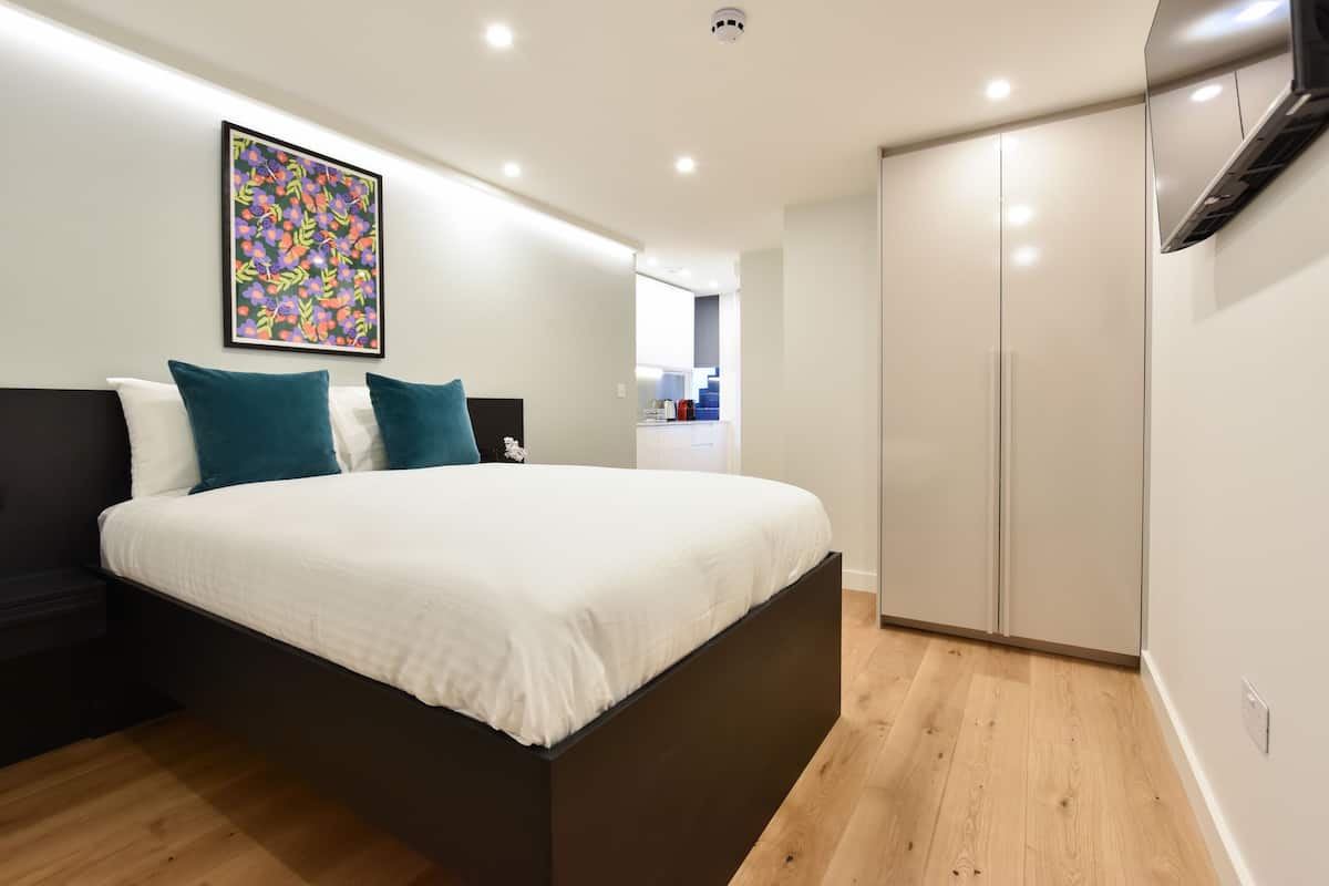 Een moderne slaapkamer met een groot bed, nachtkastje, garderobe en een televisie die aan het plafond is bevestigd.