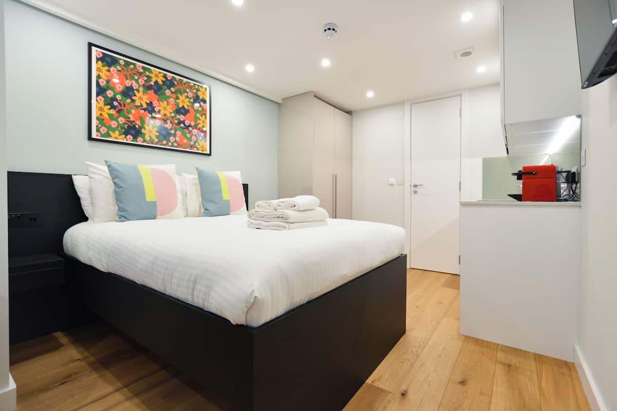 Een moderne hotelkamer met een groot bed, nachtkastje, wandtelevisie en een badkamer met spiegel en rode kast.