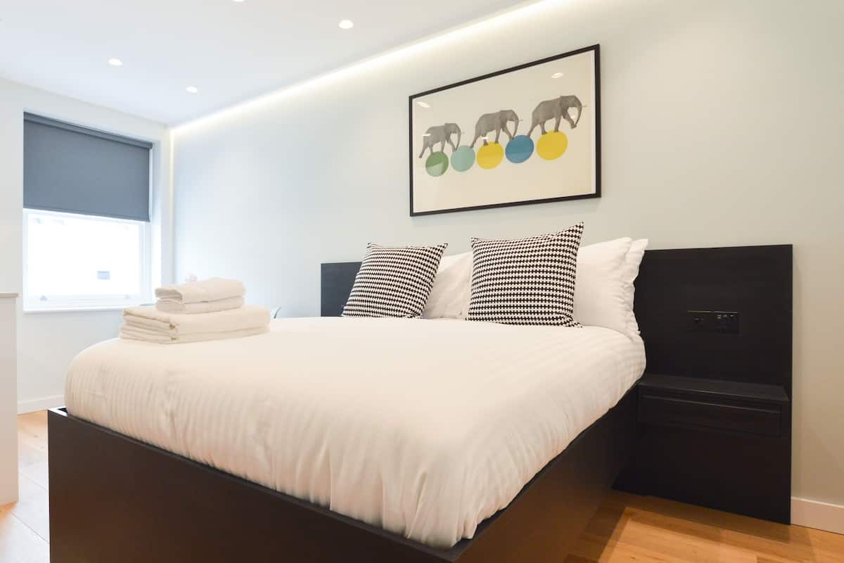 Een moderne slaapkamer met een groot bed, een hoofdbord, nachtkastje en een kunstwerk aan de wand.
