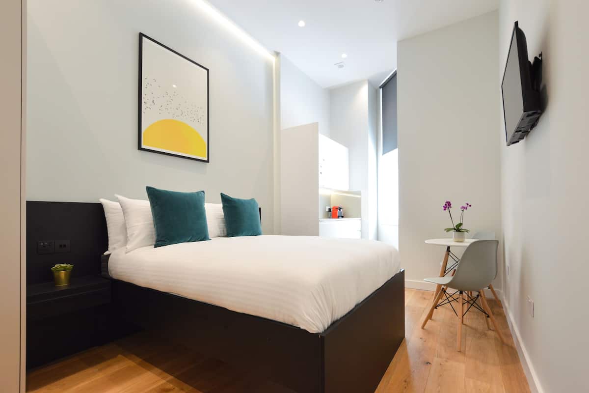 Een moderne slaapkamer met een bed, nachtkastje en een klein bureau met stoel.