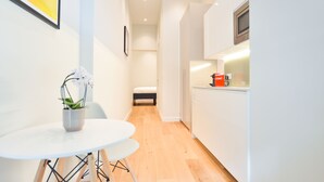 A modern, compact kitchen with a dining area, a small bed, and a potted plant. - StayPrime Earls Court Serviced Apartments (London)