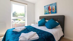 Een slaapkamer met een bed, een raam, een schilderij en een nachtkastje.