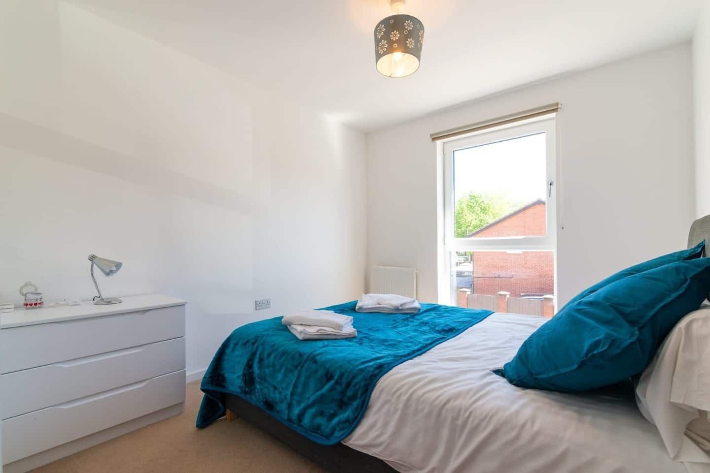 A bedroom with a bed, a desk, and a window.