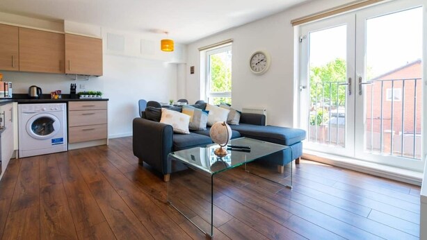 Een modern appartement met een keuken, zithoek en grote schuifpuien naar een balkon.