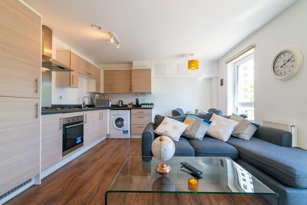 Une cuisine moderne avec des meubles en bois, un lave-linge et un coin repas comprenant un canapé et une table basse en verre.