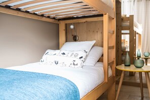 A cozy wooden room with a bunk bed, a small table with vases, and a window with curtains.
