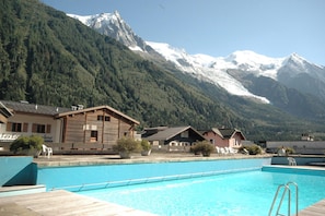 Une piscine entourée d’un paysage montagneux, avec des bâtiments en bois et un ciel dégagé.