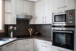 A modern kitchen with light wood cabinets, a stainless steel range hood, a built-in microwave, and an oven.