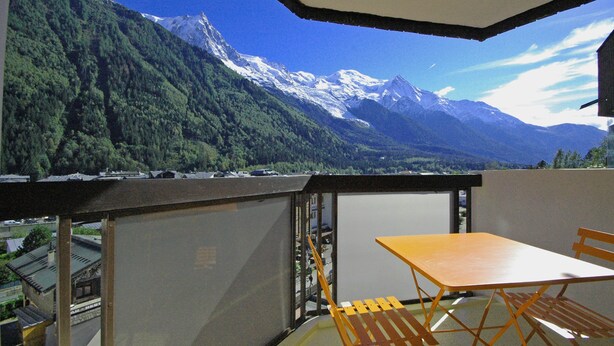 Un balcone con tavolo e sedie, affaccia su un paesaggio montuoso con cime innevate.