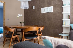 A dining area with a wooden table and chairs, a potted orchid, and a white shelf with books and decorative items. - Le Beausite C Apartment, Skiing, Chamonix All Year (Chamonix-Mont-Blanc)
