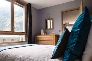 Une chambre à coucher avec un lit, une commode, un miroir et une fenêtre donnant sur les montagnes.