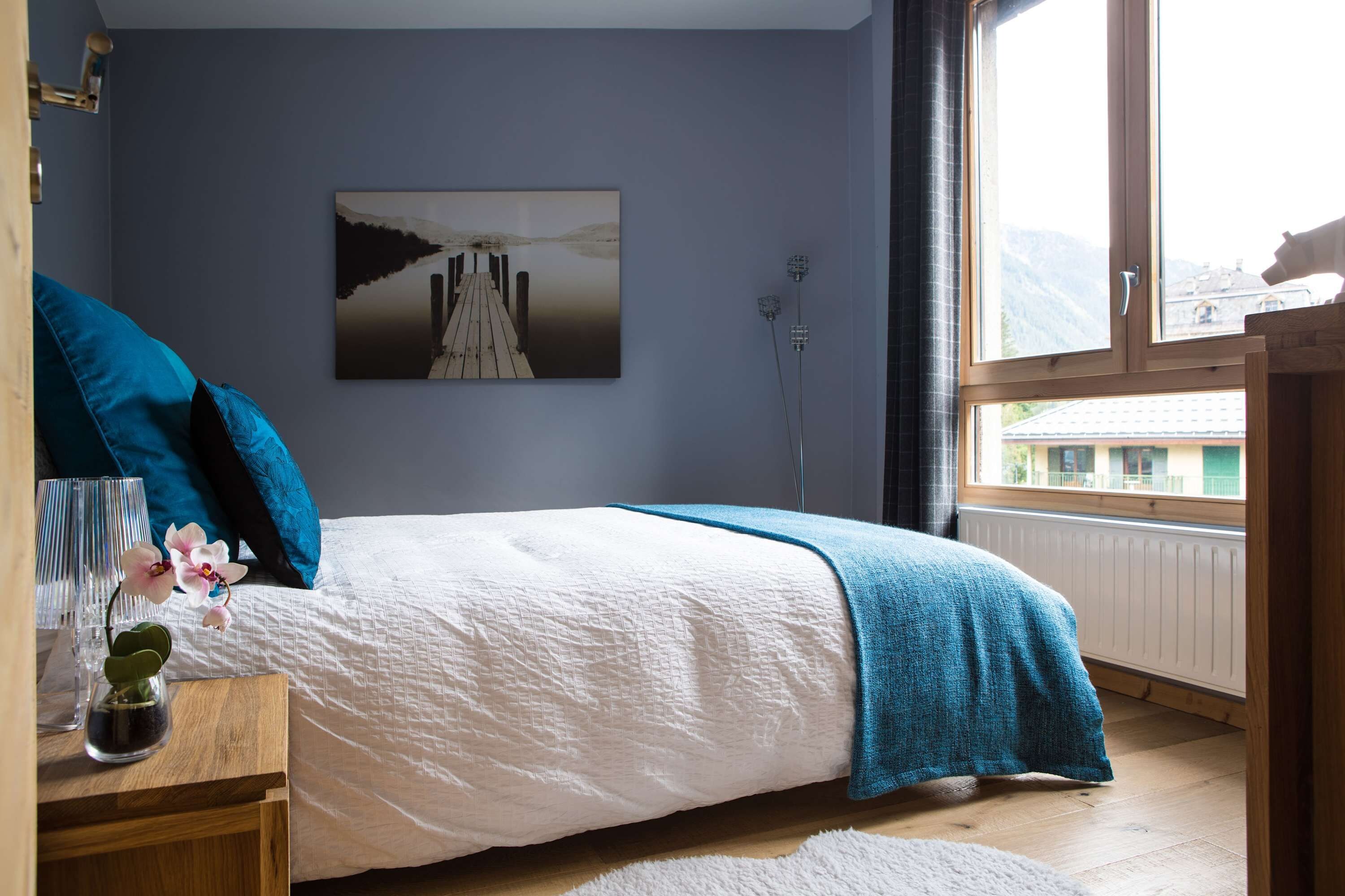 Een slaapkamer met een bed, nachtkastje, raam en een schilderij aan de muur.